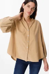 Camisa de pana color beige, con cuello mao, cierre frontal con botones y mangas largas abullonadas con puños elásticos.
