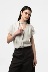 Camisa gris de corte relajado, con escote en V y lazo largo incorporado en el cuello. Mangas cortas con vuelta y frunce sutil en los hombros.