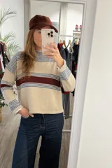 Sweater de punto corto con diseño a rayas horizontales en tonos beige, azul y bordó. Presenta cuello redondo y mangas largas con puños ajustados.