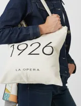 Tote bag de tela color crudo con estampado tipográfico negro en el frente que dice 1926 y La Opera. Cuenta con asas largas para llevar al hombro.