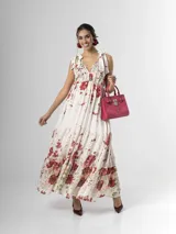 Vestido largo confeccionado en mezcla de tencel y lino, con fondo off white y estampado floral en tonos rosados, rojos y verdes. Cuenta con escote en V pronunciado, breteles anchos ajustables con lazos en los hombros, corte bajo el busto y falda amplia con volados escalonados.
