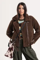 Chaqueta tipo gamulán de textura de corderito en color marrón, con cierre frontal, solapas amplias y detalles de correas ajustables en la cintura y mangas.