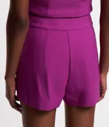 Short corto femenino de cintura alta, color fucsia, confeccionado en bengalina con cierre lateral por cremallera y detalle de pliegues (frisos) en la parte delantera.