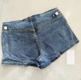 Short de denim azul tiro bajo, con diseño de doble botonadura metálica en la parte frontal y calce ajustado.