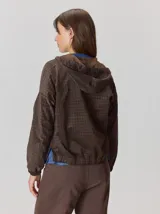 Campera de corte holgado con textura aterciopelada y estampado de cuadros sutil. Presenta cuello con cordones ajustables, cierre frontal con botones y mangas largas con puños elásticos.