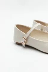 Balerinas color crudo de símil cuero texturizado, con punta redondeada, tira sobre el empeine y hebilla metálica ajustable.