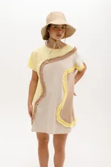 Vestido corto de algodón, con bloques de color en tonos pastel (amarillo claro, beige y rosado pálido) unidos por volados fruncidos en tonos marrón claro y amarillo. Presenta cuello redondo y mangas cortas.