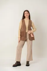 Chaleco de cuero marrón con diseño sin mangas, corte recto y bolsillos frontales con detalle metalizado en tono cobre. Presenta costuras decorativas en los bordes y en los bolsillos.