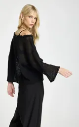 Blusa negra de punto calado con diseño amplio y transparente, escote de hombros descubiertos, mangas largas y puños acampanados.