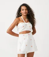 Blusa corta blanca de algodón con bordado de palmeras color naranja, escote halter y espalda descubierta.