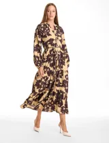 Vestido maxi de crepe con estampado floral en tonos beige y marrón oscuro. Presenta escote en V con botones frontales, mangas largas amplias con puños abotonados y cintura ajustable mediante cordón trenzado. La falda cuenta con un diseño de vuelos escalonados que aporta movimiento.