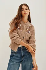 Cardigan de punto grueso en color azul, con cierre frontal de botones, mangas largas con puños de encaje blanco y detalle de bordado floral con pedrería brillante en el pecho.