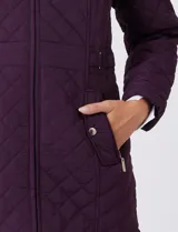 Campera capitoneada de largo midi en color bordó, con diseño de rombos en el cuerpo y mangas, y costuras diagonales en los laterales. Cuenta con cierre frontal, capucha desmontable con interior suave y panel entallado en la cintura.