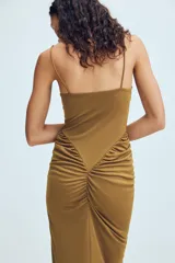 Vestido largo color tostado con diseño estilo corsé, escote corazón con aros y tirantes finos. Presenta un corte ajustado en la cintura con detalle de frunces laterales que aportan volumen a la falda.