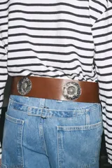 Cinturón ancho de cuero marrón con hebilla cuadrada metálica y apliques de flores metálicas plateadas.