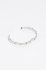 Pulsera rígida plateada con cierre de bisagra, decorada con incrustaciones en forma de corazón con pequeños cristales.
