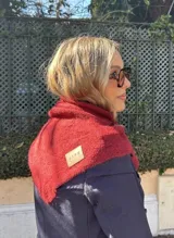 Bufanda de punto con diseño triangular en color marrón oscuro, con detalle de etiqueta de cuero sintético en una esquina.