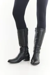 Bota de caña alta de cuero liso negro, con diseño clásico, detalles de hebillas metálicas, cierre lateral y taco bajo.