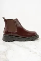 Bota Chelsea de cuero color marrón oscuro con elásticos laterales y suela track negra.