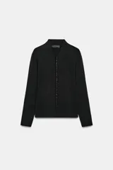 Chaqueta de punto negro con escote en V y manga larga. Cierre frontal con una hilera de pequeños botones forrados.