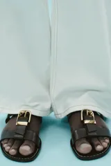 Sandalia plana color marrón con doble tira y hebilla metálica dorada.