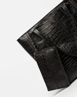 Bolso shopper negro de cuero con textura de cocodrilo, doble asa de hombro y dije colgante rectangular.