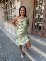 Conjunto de dos piezas compuesto por un top de un solo hombro con volados y una falda corta con ruedo asimétrico, confeccionado en tela satinada con estampado floral en tonos verde y dorado.