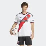 Camiseta de fútbol Adidas del River Plate, modelo local, color blanco con la característica banda diagonal roja, detalles en negro y cuello redondo.