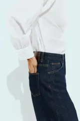 Camisa blanca de manga larga con cuello de solapa y detalles de encaje a tono en el cuello y los puños. Presenta cierre frontal con botones y corte recto.