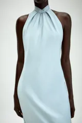 Vestido midi de satén color celeste, con cuello halter y detalle de lazada en la espalda descubierta.