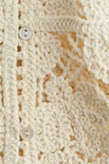 Chaleco sin mangas de punto crochet color crema, con diseño floral calado y ribetes de picot en cuello, sisas y ruedo. Cierre frontal con botones nacarados.