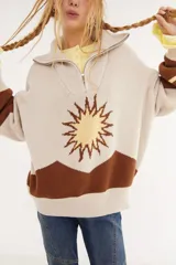 Sweater de punto en color beige con diseño de intarsia que representa un sol y montañas en tonos marrón y amarillo. Presenta cuello alto con cierre frontal, mangas largas y corte holgado.