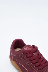 Zapatilla de estilo barefoot color marrón, confeccionada con una combinación de gamuza y materiales sintéticos. Presenta un diseño de perfil bajo con suela de goma flexible en color caramelo que incluye el logo de la marca grabado en el lateral.