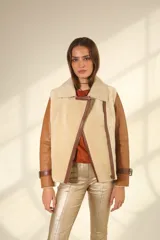 Chaqueta tipo gamulán de cuero color camel con interior y solapas de piel sintética en color beige. Presenta cierre frontal cruzado, correas ajustables con hebillas en los puños y en los laterales de la cintura.