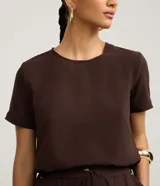 Blusa fucsia de manga corta con cuello redondo pespunteado, diseño sin estampa y efecto airflow con textura sutil. Cuenta con abertura trasera tipo gota y cierre con botón.