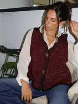 Chaleco tejido color tostado con destellos de lurex, escote en V y cierre frontal con botones. Presenta detalles de bordados y terminaciones en crochet en color crudo.