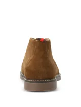 Botas tipo chukka Hush Puppies modelo New Safari, confeccionadas en descarne color marrón tostado. Presentan cordones al tono, costuras reforzadas en la suela y detalle de etiqueta con franjas en el talón.