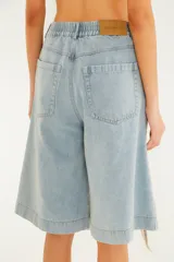 Bermuda de jean de tiro alto en color celeste, con diseño amplio y largo por la rodilla. Presenta detalles calados con bordados artesanales y aberturas que dejan ver secciones de red en tono crudo, además de bolsillos laterales y cintura elástica en la parte trasera.