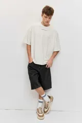 Remera oversize de color blanco marfil, de corte holgado, manga corta y cuello redondo, con un pequeño estampado tipográfico en el centro del pecho.