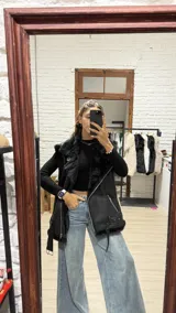 Chaleco estilo gamulán negro, con interior y solapas de piel sintética al tono. Presenta cierre frontal cruzado, bolsillos laterales con cierre y cinturón ajustable en el ruedo.