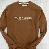 Buzo marrón de algodón con felpa, cuello redondo y puños y cintura acanalados. Estampado frontal con la inscripción "Duxon Jeans Los Angeles Est 1982" en color blanco.