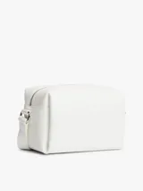 Cartera bandolera blanca Tommy Jeans de poliuretano, diseño cuadrado con cierre de cremallera y compartimento principal. Cuenta con correa ajustable, insignia metálica con el logo de la marca en el frente y un colgante lateral extraíble de cordón rojo trenzado con argollas metálicas.