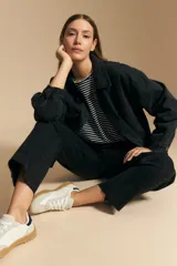 Jean de corte recto y tiro medio, confeccionado en denim elastizado de color negro. Presenta un diseño clásico con cierre de botón y cremallera, bolsillos laterales y traseros, y ruedo con terminación deshilachada.