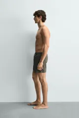 Bañador de hombre de largo medio, color celeste claro con rayas blancas horizontales. Presenta cintura elástica ajustable con cordón, bolsillos frontales y bolsillos traseros de plastrón. Incluye forro interior.