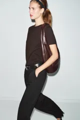 Bolso de hombro tipo saca en formato maxi, confeccionado en material sintético negro. Presenta un diseño holgado con asa integrada, cierre imantado en el compartimento principal, bolsillo lateral con cremallera y detalle de tirador.