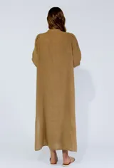 Vestido largo color beige de lino, con cuello mao, mangas 3/4 abullonadas y cierre frontal con botones. Presenta volantes verticales en el frente.
