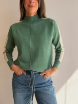 Sweater de tejido de punto en color beige con cuello alto y costura central vertical. Presenta mangas ranglan con una franja lateral en color marrón oscuro que genera contraste, y terminaciones en tejido acanalado en puños y ruedo.