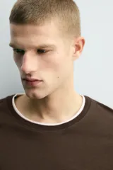 Camiseta de manga larga y corte relajado en color marrón oscuro. Presenta un diseño de doble capa en el cuello y el ruedo, con un borde interior en color blanco que crea un efecto de contraste.