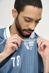 Camiseta de fútbol celeste con rayas verticales, cuello polo y mangas 3/4 con puños blancos. Incluye el número 78 en el frente y logos estampados.