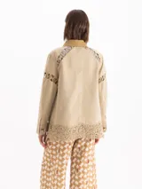 Chaqueta de gabardina liviana color verde militar, con silueta recta, largo por debajo de la cadera y cuello de corderoy. Presenta detalles de encaje en hombros, mangas y ruedo, múltiples bolsillos con solapa y cierre frontal con broches metálicos.